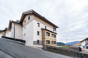A multi-story building with a flat roof, a stone wall in front, and a paved road in the foreground.