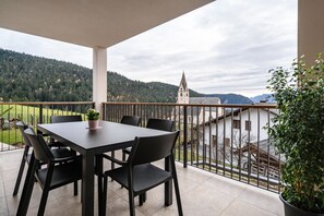 Un balcon avec une table et des chaises, un pot de fleurs et une vue sur une église et des montagnes.