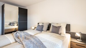 A modern bedroom with a large bed, bedside tables, a mirror, and a nightstand. - Apartment 'Klara' with Mountain View, Private Terrace and Wi-Fi (Mölten)
