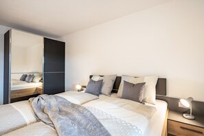 A modern bedroom with a large bed, bedside tables, a mirror, and a nightstand.
