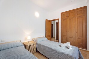 A bedroom with two single beds, a wooden wardrobe, a bedside table with a lamp, and a small wooden basket. - Apartment 'Noa' with Wi-Fi (San Sebastián de La Gomera)