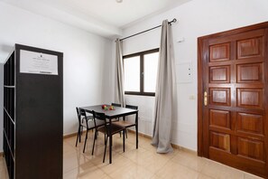 A room with a wooden door, a window with curtains, a table with chairs, and a black cabinet. - Apartment 'Noa' with Wi-Fi (San Sebastián de La Gomera)