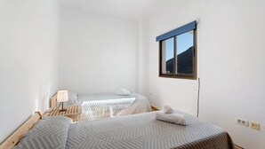 A room with two beds, a small table with a lamp, and a window with a view of a mountain. - Apartment 'Noa' with Wi-Fi (San Sebastián de La Gomera)