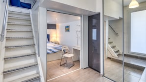 Un intérieur moderne avec un escalier, un lit recouvert d’une couverture à rayures, une chaise et une porte vitrée donnant sur une autre pièce.