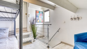 Une pièce avec des lits superposés, un canapé bleu, un escalier, une plante en pot et une œuvre d’art colorée accrochée au mur.