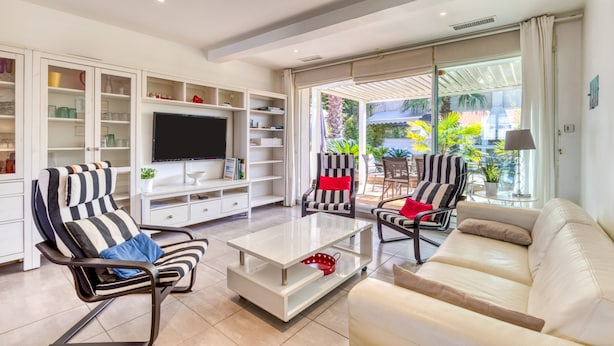 Un salon moderne avec un téléviseur, des fauteuils à rayures, un canapé blanc et une porte en verre donnant sur un espace extérieur.