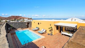 A pool area with lounge chairs, a table, and a view of the sea. - Vacation Home "Finca Acequia" with Sea View, Private Pool & Wi-Fi (Tinajo)