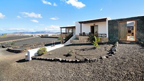 A modern house with a stone facade, a wooden door, and a view of mountains. - Vacation Home "Finca Acequia" with Sea View, Private Pool & Wi-Fi (Tinajo)