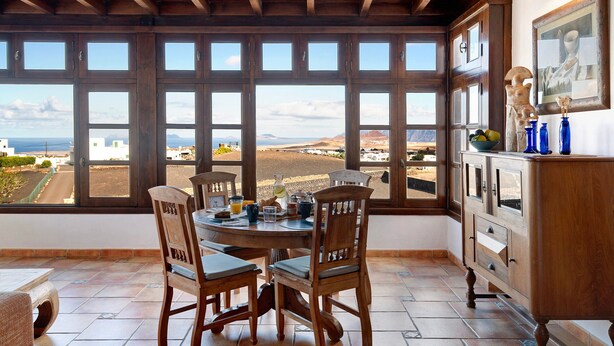 A dining area with a table, chairs, and a view through large windows. - Vacation Home "Finca Acequia" with Sea View, Private Pool & Wi-Fi (Tinajo)