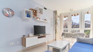 Ein modernes Wohnzimmer mit Fernseher, weißen Schränken, einer Couch und einem Balkon mit Blick.