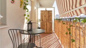 Ein Balkon mit Tisch und Stühlen, eine Holztür und ein gestreifter Sonnenschirm.