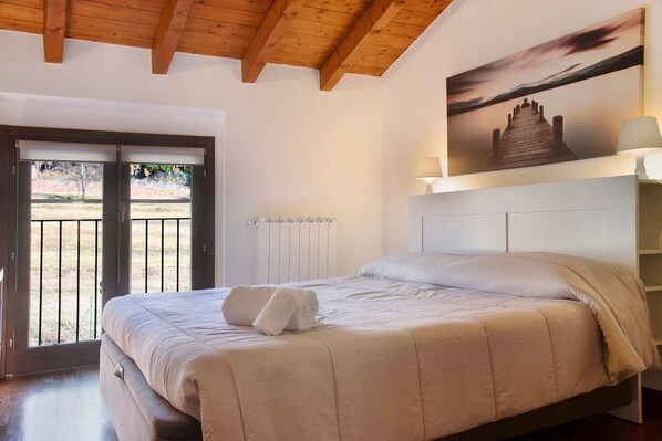 Une chambre à coucher avec un lit, un tableau, une lampe et une vue sur l’extérieur, visible à travers une porte.