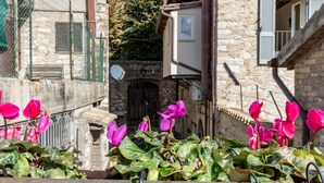 A stone building with a balcony, a metal fence, and pink flowers in the foreground.