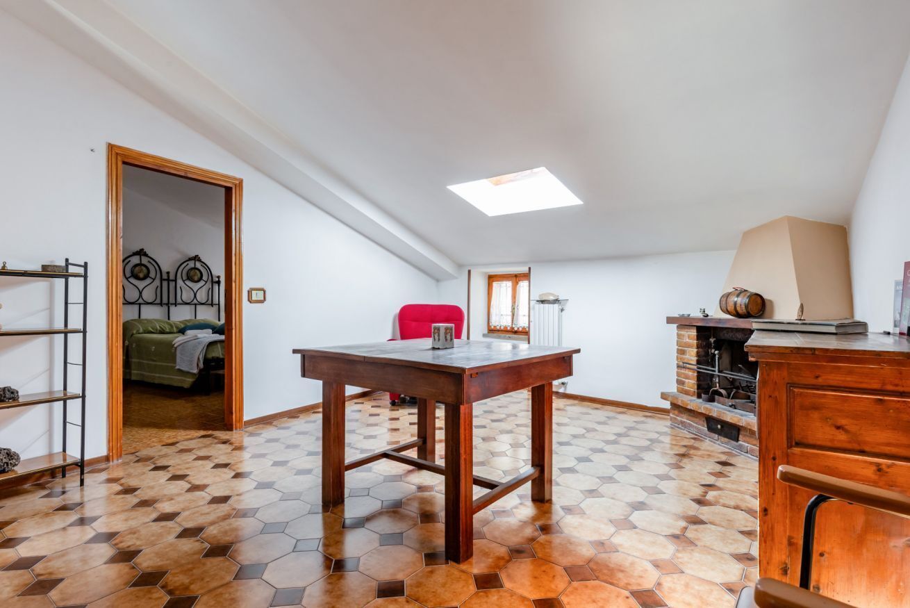 A room with a wooden table, a red chair, a bookshelf, a bed, and a fireplace.