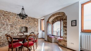 A dining area with a stone wall, a chandelier, a round table, and red upholstered chairs.