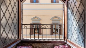 A balcony with a wrought iron railing, stone walls, and a view of buildings with shutters.