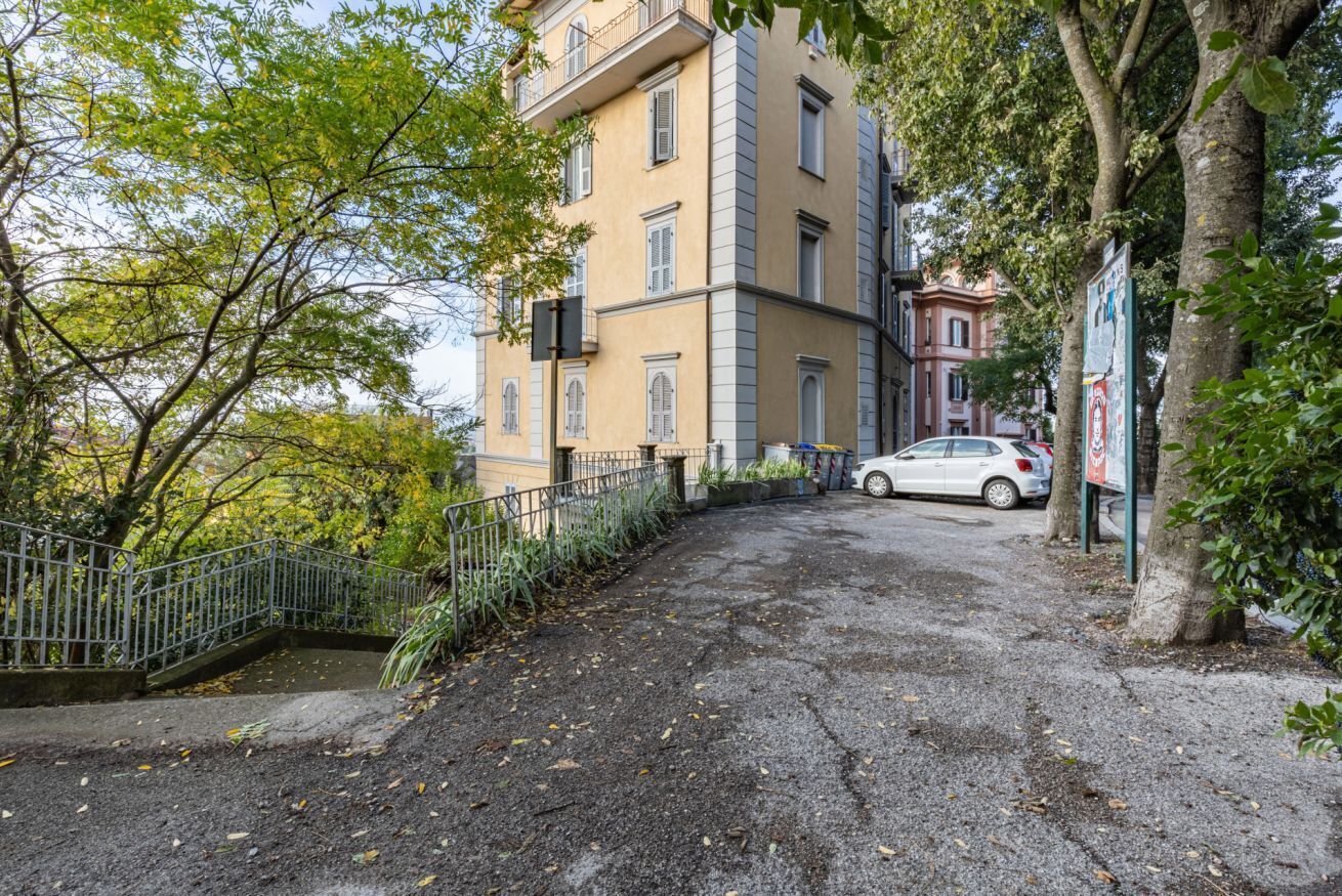 Un edificio con ingresso pavimentato, recinzione in metallo e un'auto parcheggiata.