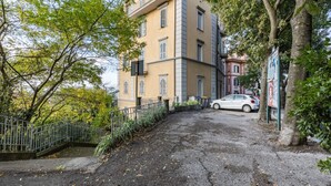 A building with a paved entrance, a metal fence, and a parked car. - GuestHost - Cozy apartment equipped with all comforts to accommodate 4 people, with 2 bedrooms, 2 bathrooms and private garden. Located in an elegant period building in Art Nouveau style, it is outside the restricted traffic zone, but just a 10-minute wa (Perugia)