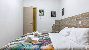 A hotel room with a bed, a headboard, a door, and a wall with a stone accent. - GuestHost - Cozy apartment equipped with all comforts to accommodate 4 people, with 2 bedrooms, 2 bathrooms and private garden. Located in an elegant period building in Art Nouveau style, it is outside the restricted traffic zone, but just a 10-minute wa (Perugia)