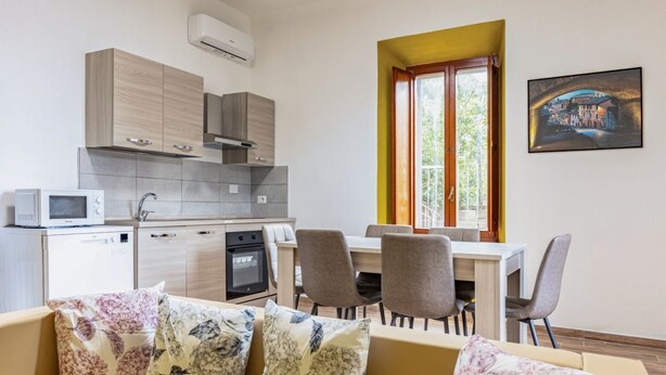 A modern kitchen with grey cabinets, a microwave, and a dining area with a table and chairs. - GuestHost - Cozy apartment equipped with all comforts to accommodate 4 people, with 2 bedrooms, 2 bathrooms and private garden. Located in an elegant period building in Art Nouveau style, it is outside the restricted traffic zone, but just a 10-minute wa (Perugia)