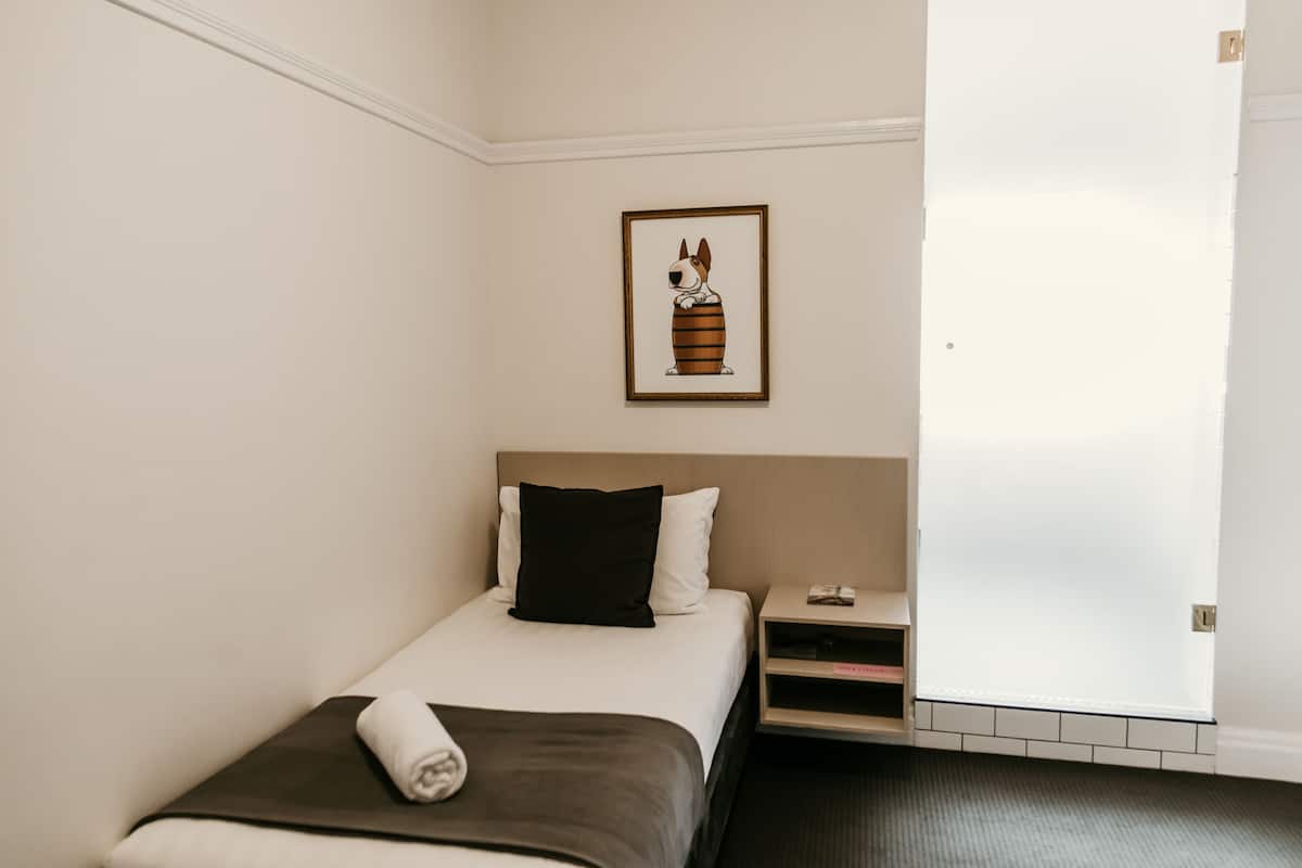 A hotel room with a single bed, a nightstand, a framed picture on the wall, and a door to the right.