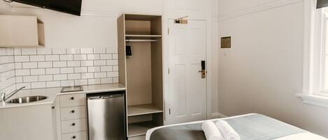 Habitación de hotel con kitchenette, una cama y una toalla doblada con cuidado, una puerta blanca y una ventana.