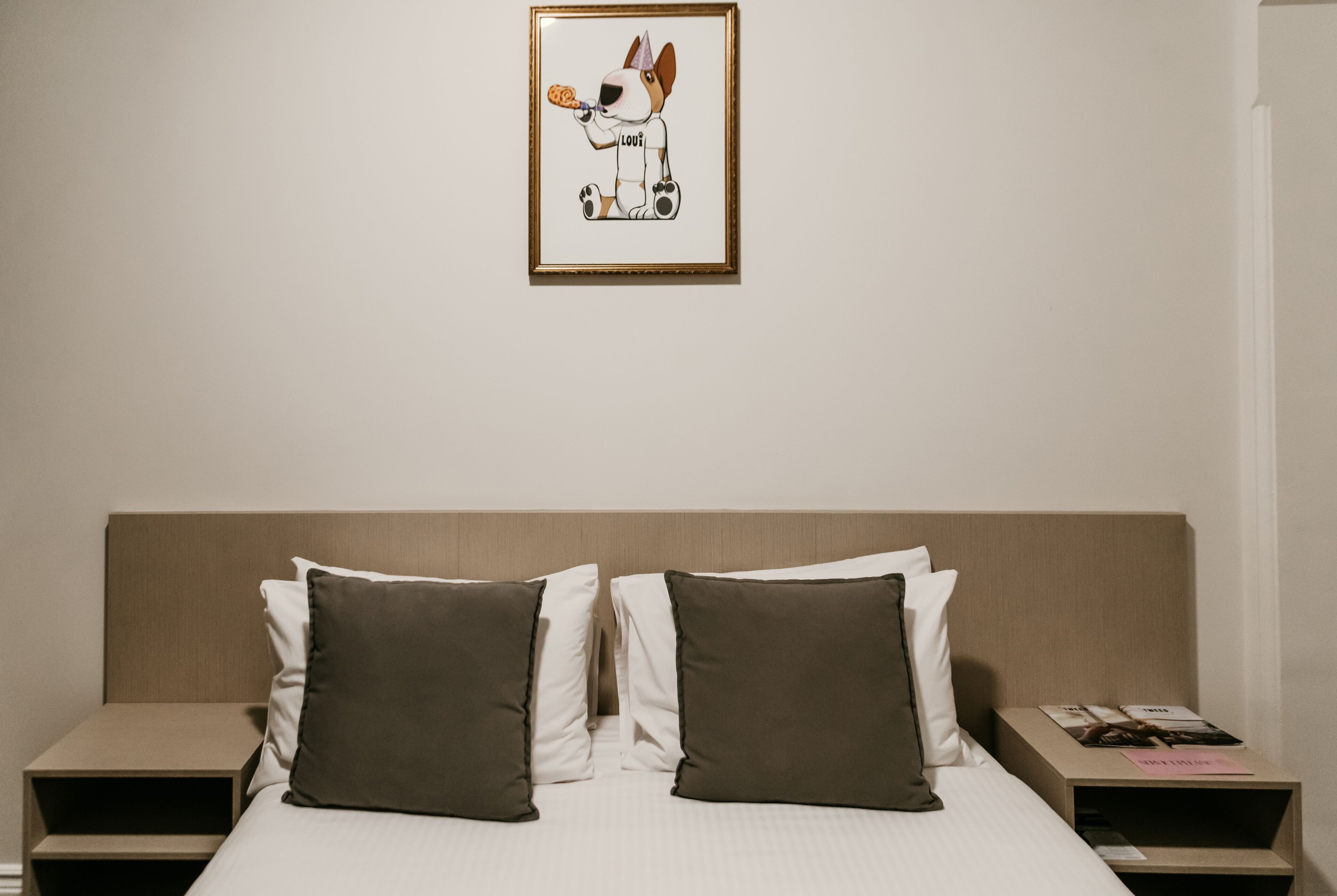 A hotel room with a bed, two nightstands, a framed picture on the wall, and a magazine on the nightstand.