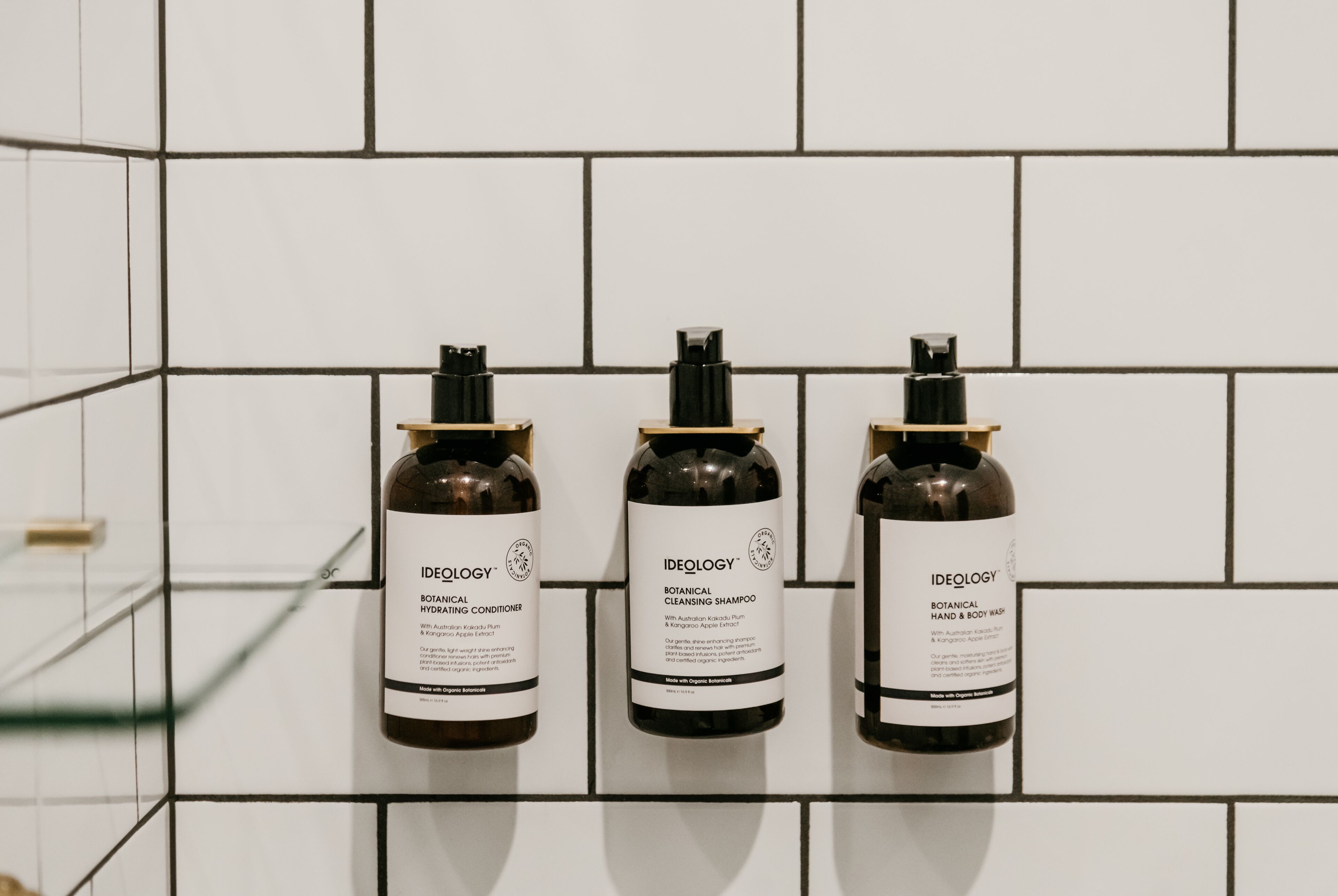 Three bottles of Ideology Botanical products on a tiled wall.