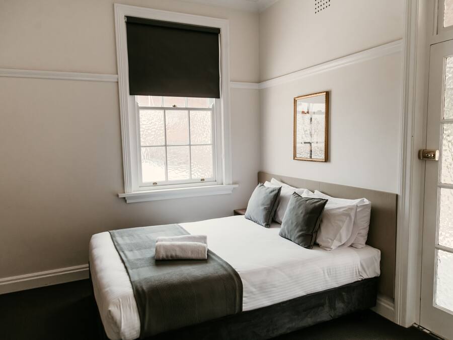 A bedroom with a bed, a window with a dark blind, a framed picture on the wall, and a door with glass panels.