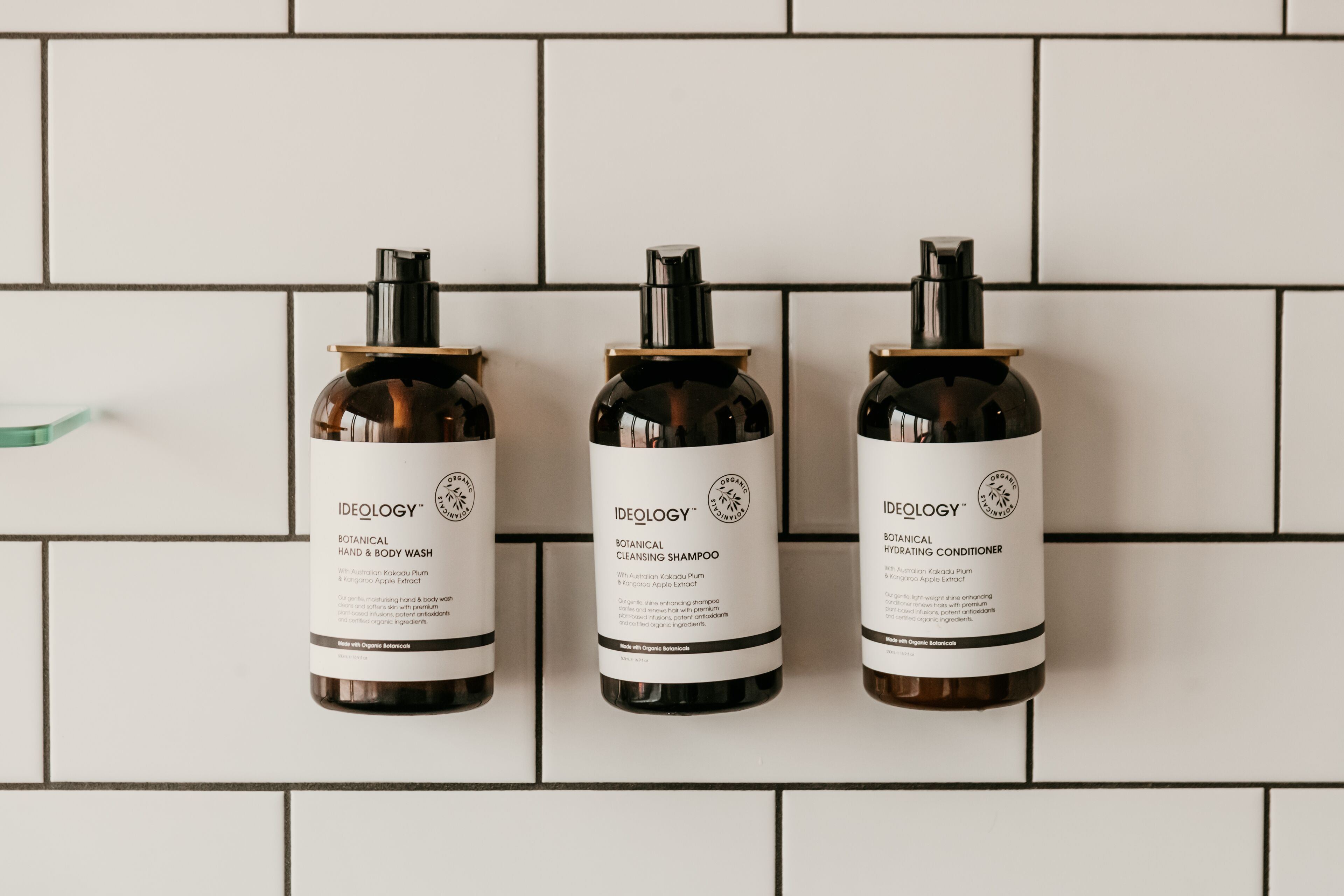 Tres botellas de productos para el cuidado de la piel Ideology sobre una pared de azulejos.