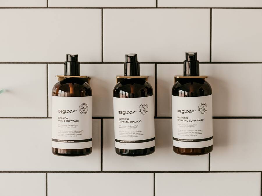 Three bottles of Ideology skincare products on a tiled wall.