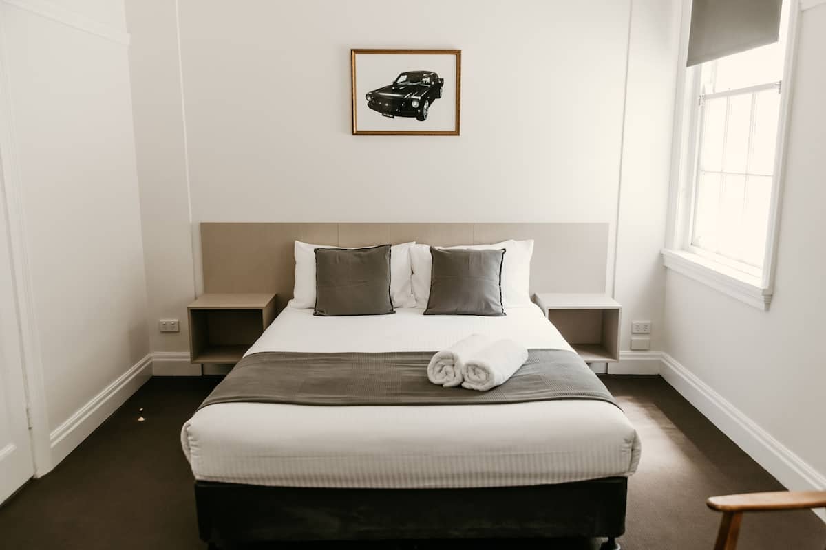 A neatly made bed with a gray blanket and two pillows, a framed picture on the wall, and a window on the right side.