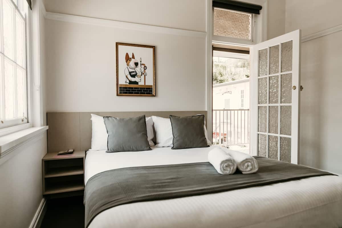 A neatly made bed with grey bedding, a framed picture on the wall, and a view through an open door.