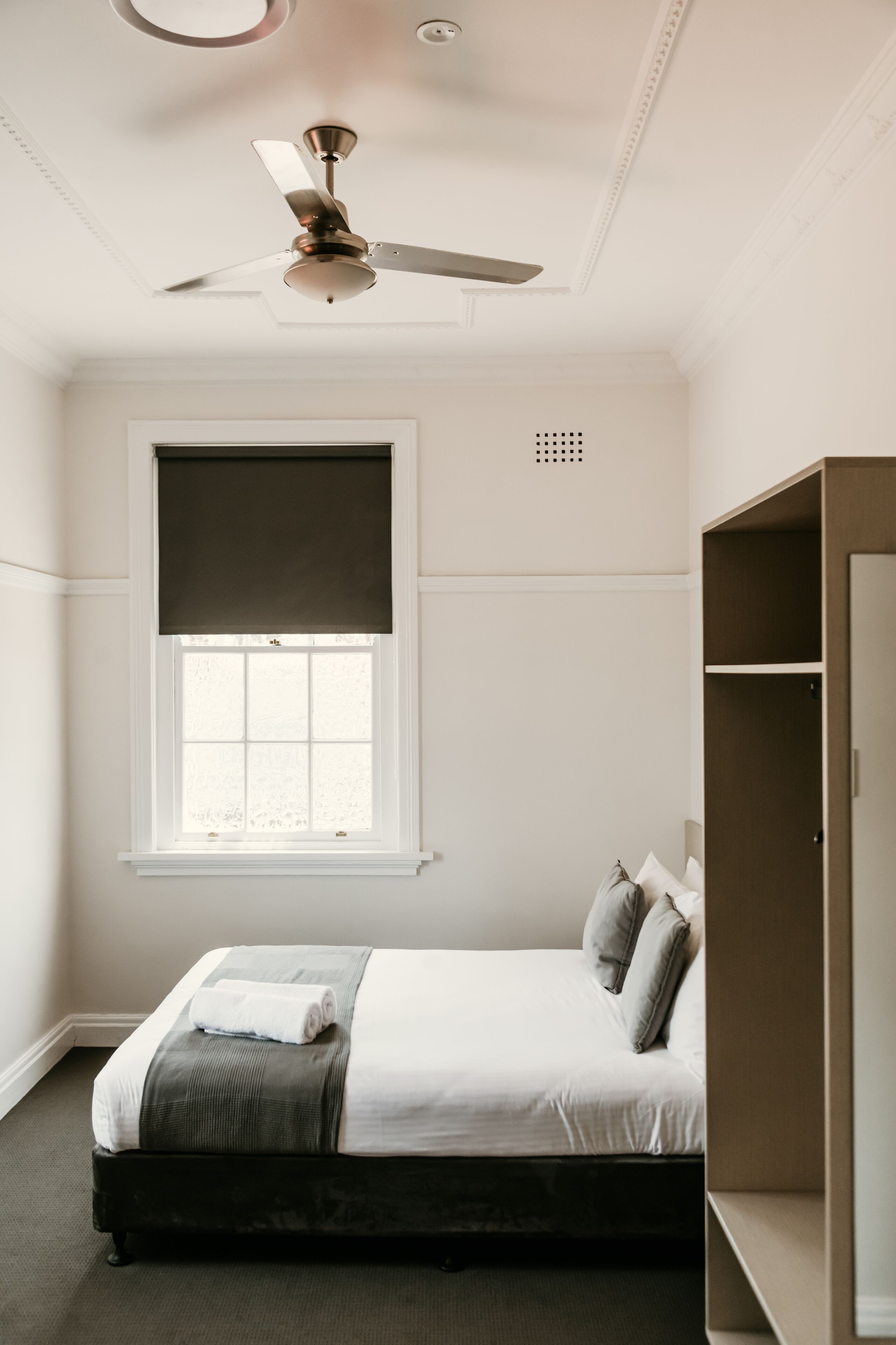 A bedroom with a bed, a ceiling fan, a window with blinds, and a wardrobe.