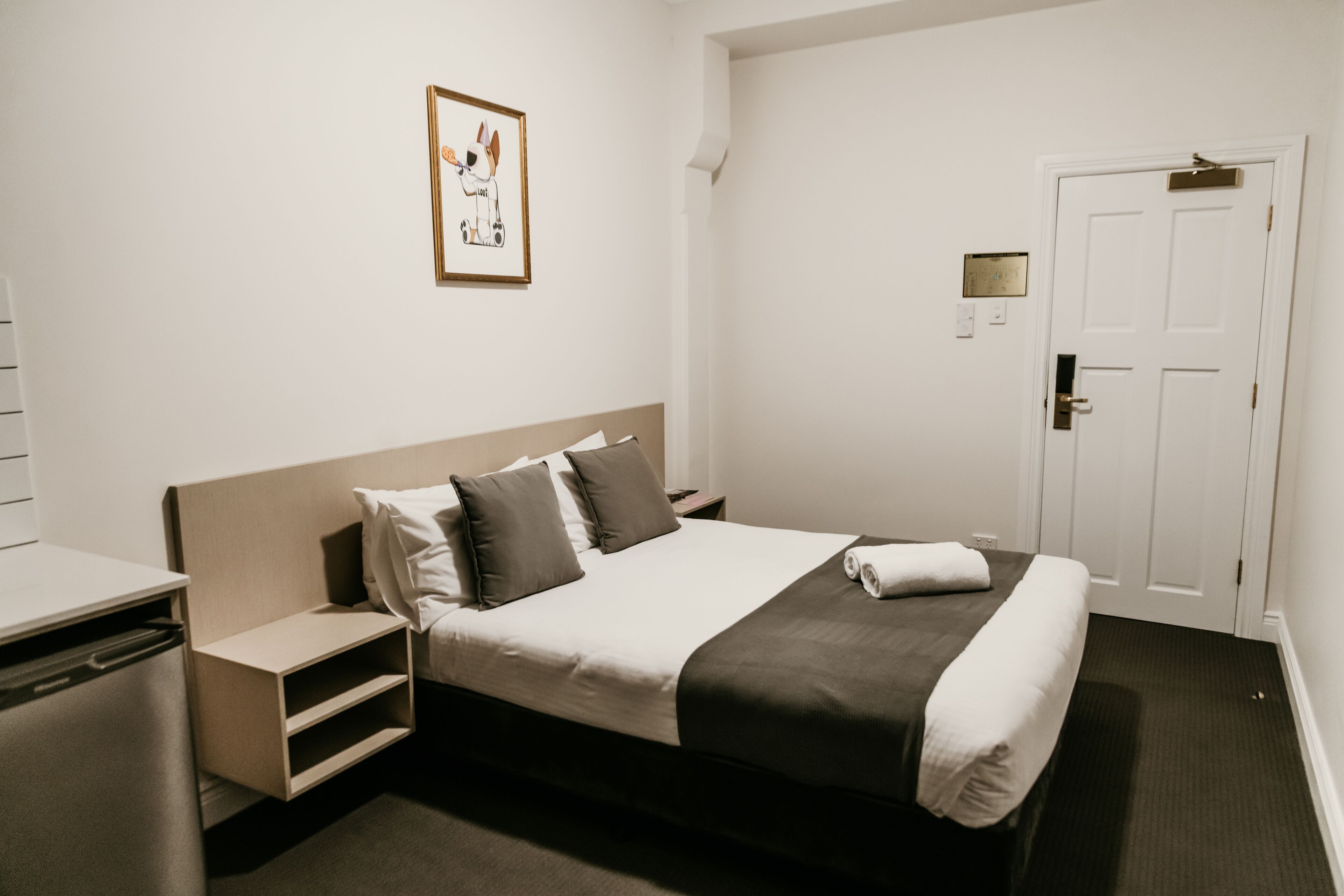 Quarto de hotel com cama, mesas de cabeceira, escrivaninha e porta.