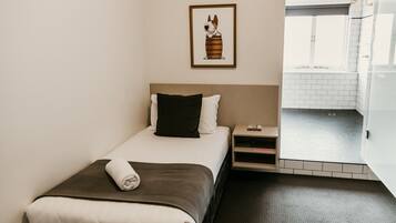 Una habitación de hotel con cama, mesita de noche, un cuadro en la pared y vistas al baño.
