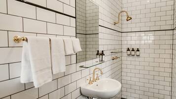 A modern bathroom with white subway tiles, a white sink, gold fixtures, and a glass shelf with toiletries.