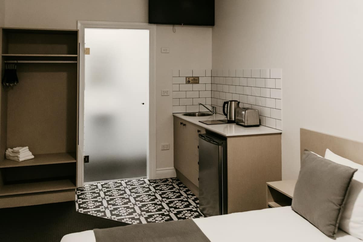 A hotel room with a bed, a desk with a kettle, a TV, and a wardrobe.