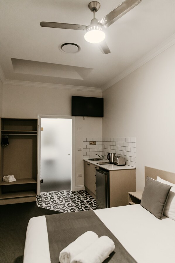 Una habitación de hotel con cama, escritorio con tetera, televisor y armario.