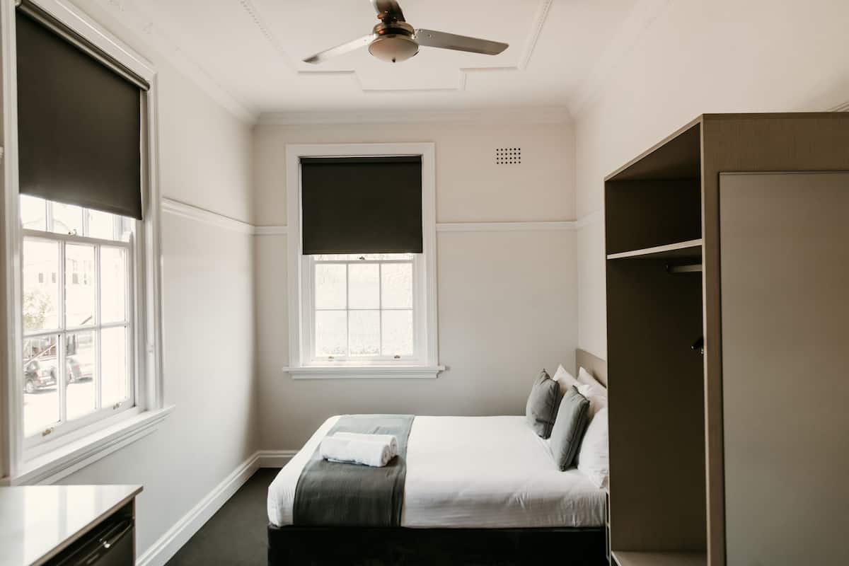 A bedroom with a bed, a ceiling fan, a window with blinds, and a wardrobe.