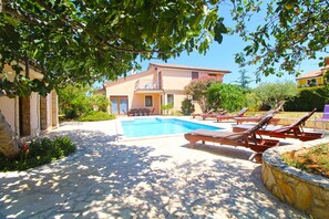 A pool area with lounge chairs, a stone pathway, and a building with a balcony. - Villa with swimming pool and barbecue area (Ližnjan)