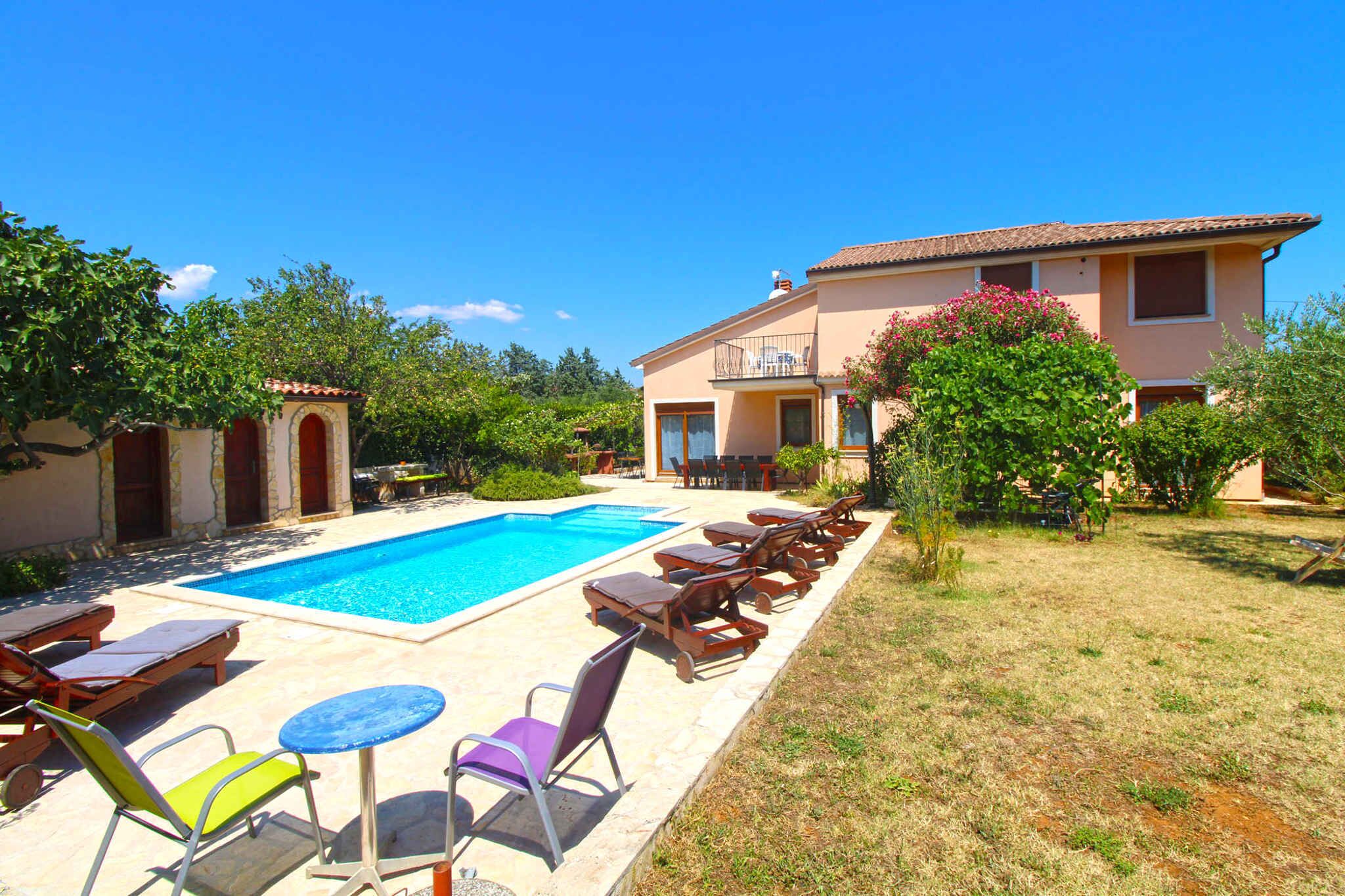 Un'area piscina con lettini e un tavolo, circondata da un giardino e un edificio con un balcone.