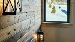 Una stanza con una parete in legno, una finestra vista paesaggio innevato e un lampione a parete.