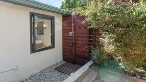 A small, private outdoor shower area with a wooden wall and a metal door, surrounded by gravel and plants. - Spanish Style Highland Park Home + Free Parking (Los Angeles)