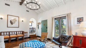 A spacious living room with a high ceiling, wooden bench seating, a leather armchair, and a red cabinet. - Spanish Style Highland Park Home + Free Parking (Los Angeles)