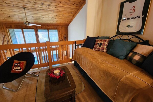 Una habitación acogedora con techo de madera, cama con muchos almohadones, una mesita con vela y flores, y un cuadro en la pared.