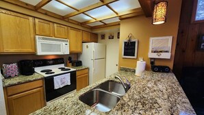 Una cocina con armarios de madera, microondas blanco, estufa, refrigerador y encimera de granito.