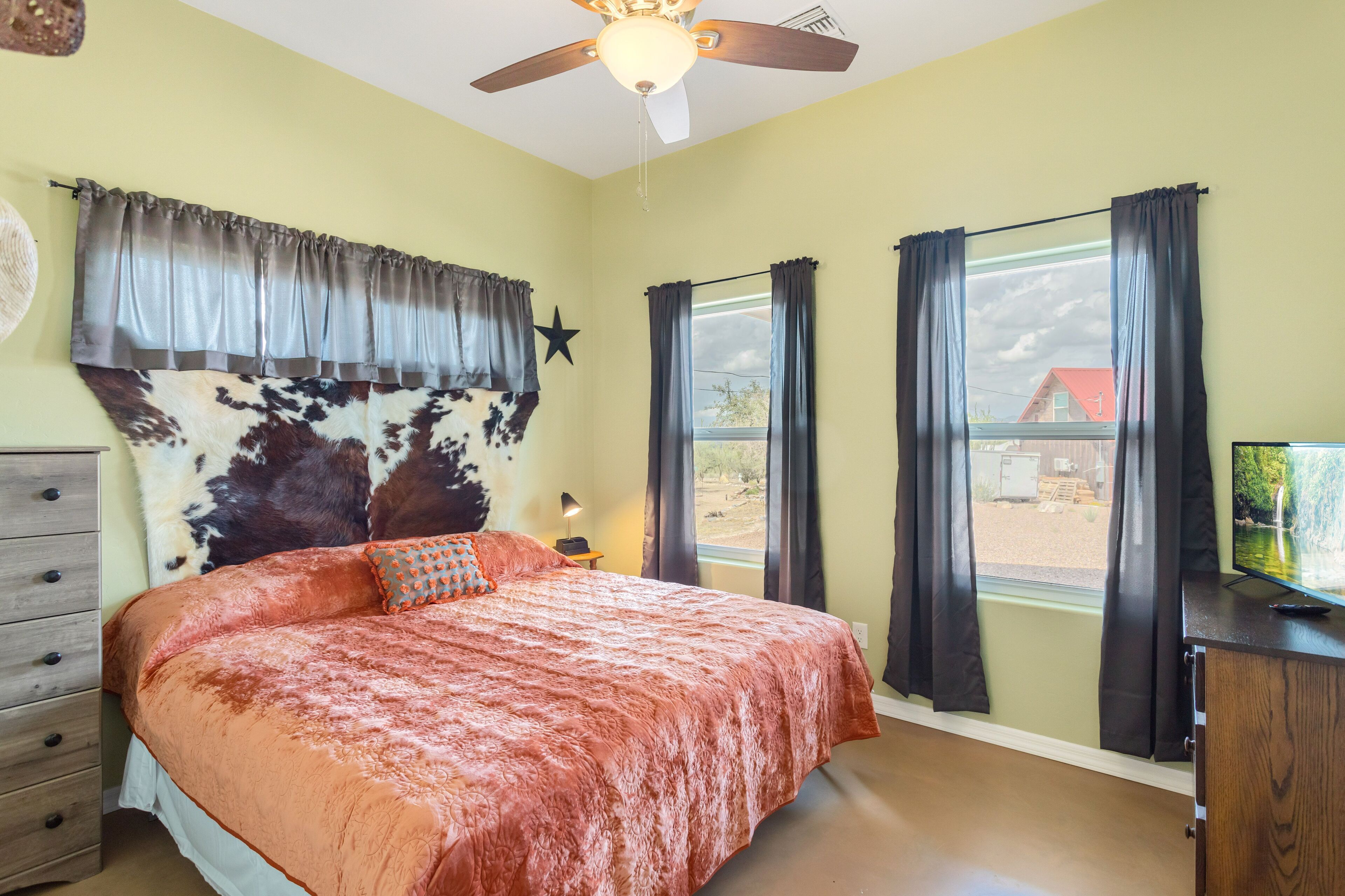 A bedroom with a large bed, a ceiling fan, a window with curtains, and a star decoration on the wall.
