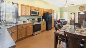 A kitchen with wooden cabinets, stainless steel appliances, and a dining area with a table set for four. - Experience the Wild West in Style: Unforgettable Getaway in Tombstone, Arizona!! (Tombstone)