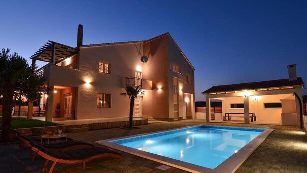 Una casa moderna de dos pisos con piscina, mobiliario exterior y un patio cubierto.
